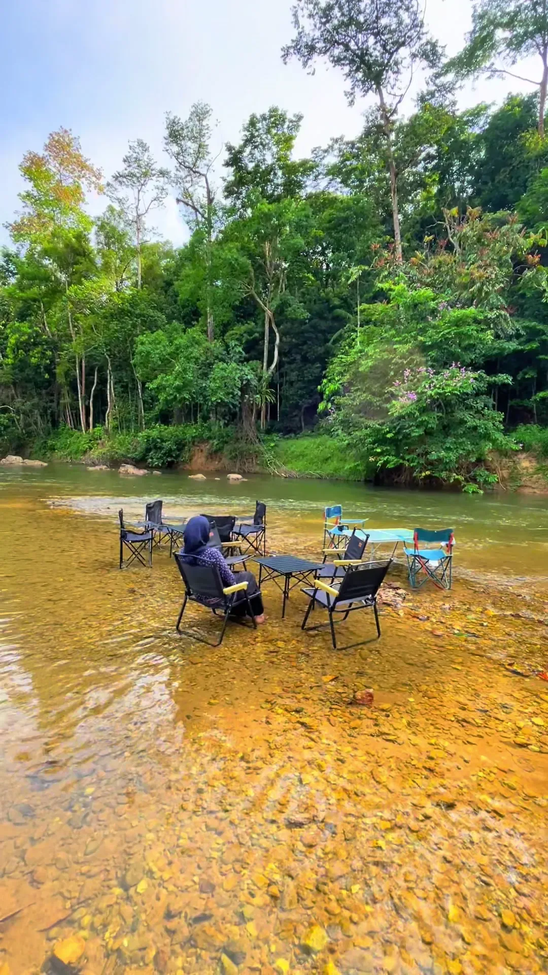 Kerusi dan meja berdiri di dalam sungai jernih Barouk Hut, hutan hijau di belakang